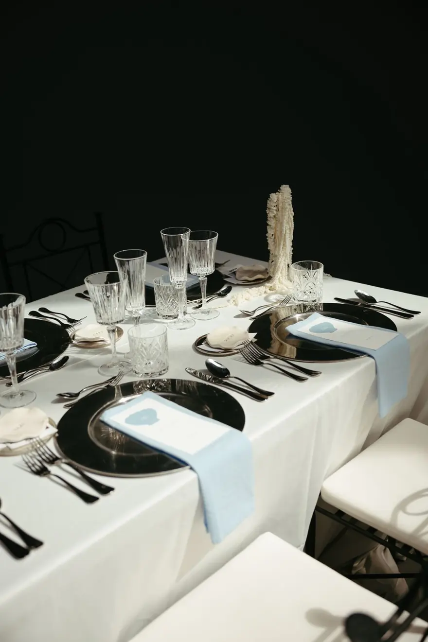 Mesa con mantel blanco, bajoplatos negros y minutas en azul